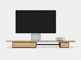 Modern monitor stand with a flat-screen apple display studio on a white backgroundoakywood wooden desk shelf pro, solid wood monitor stand side view | light oak, single drawer, black