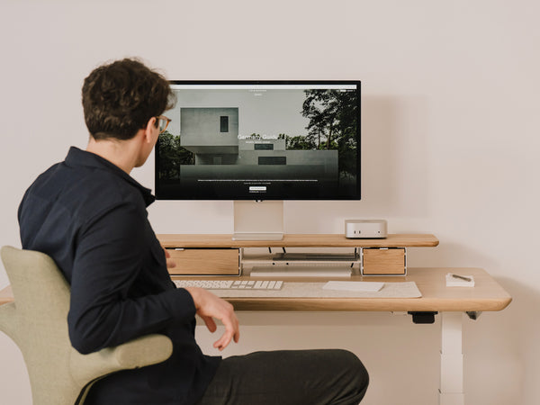 Person sitting at a desk with a Mac mini computer and apple display studio monitor displaying an image of a house. |light oak, , 