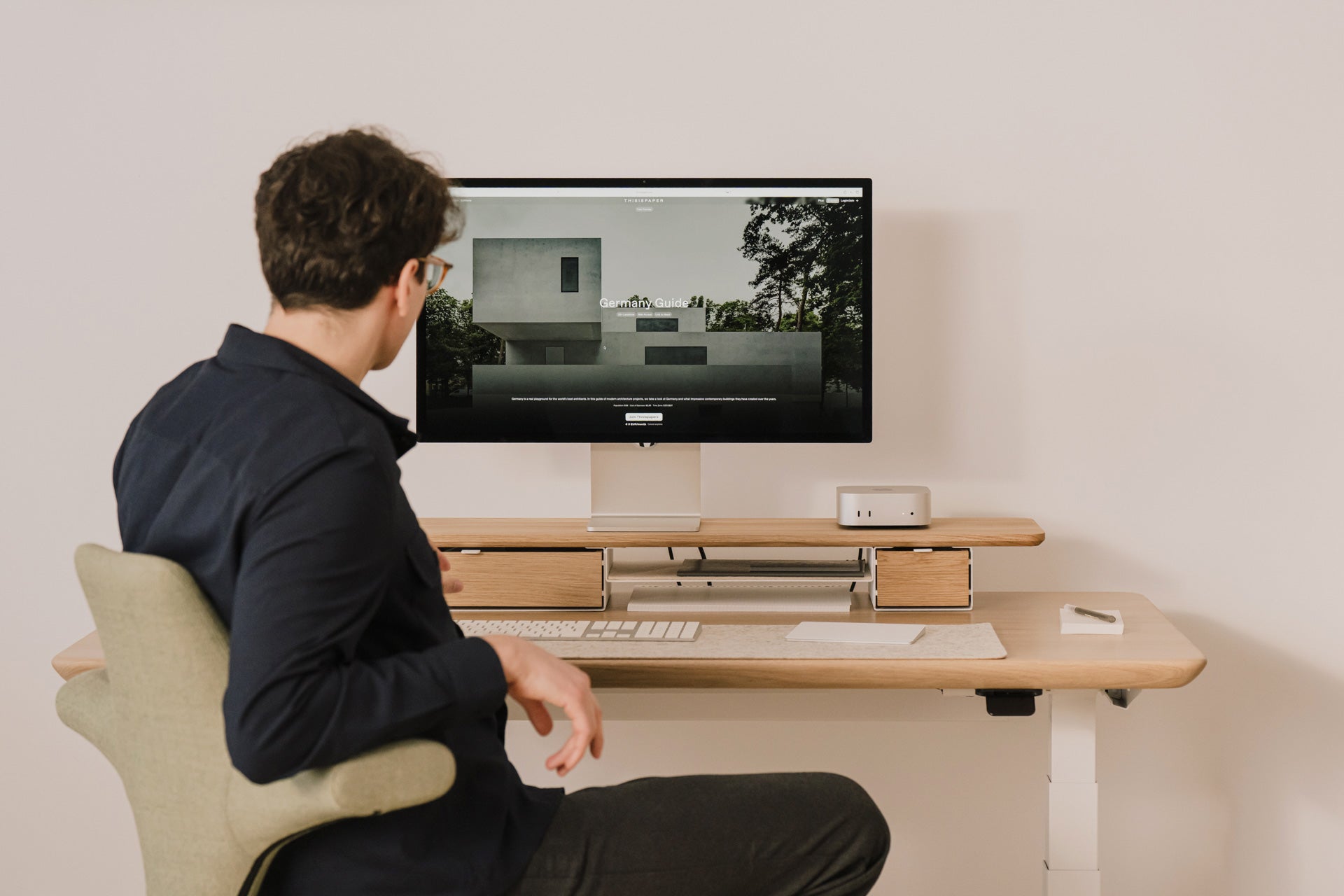 Person sitting at a desk with a Mac mini computer and apple display studio monitor displaying an image of a house. |light oak, , 