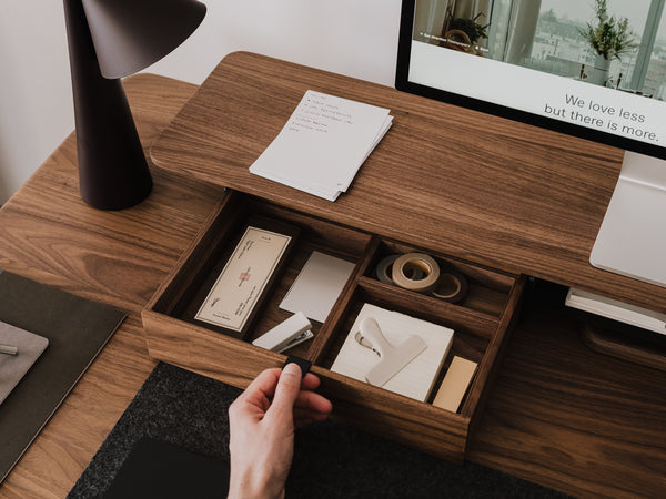 Wooden desk with open drawer containing stationery items, hand reaching in  | walnut, 