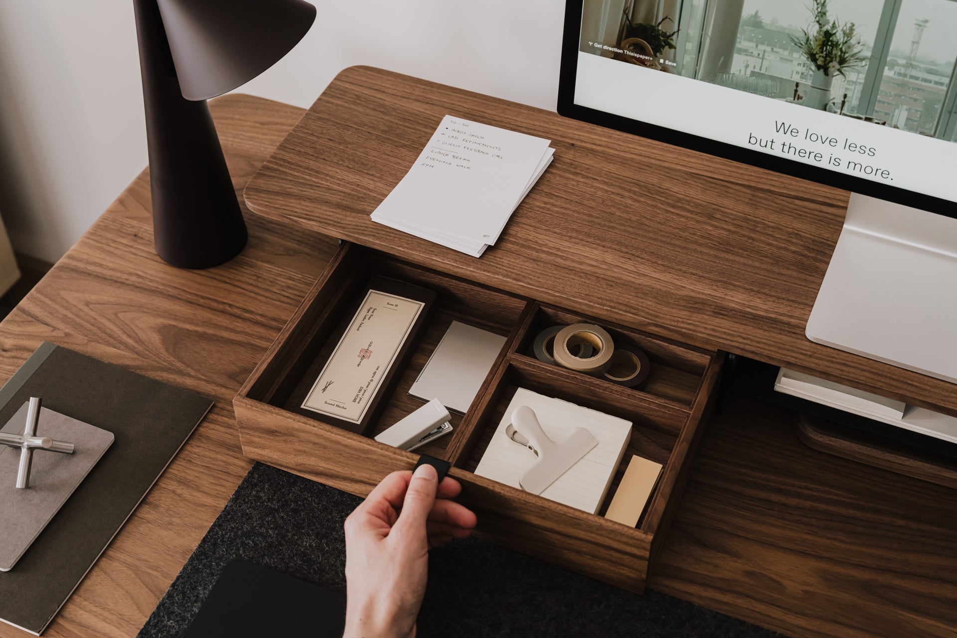 Wooden desk with open drawer containing stationery items, hand reaching in  | walnut, 
