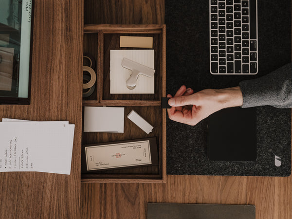 Person organizing items in a wooden desk organizer with a laptop and papers on a wooden desk. | walnut, 