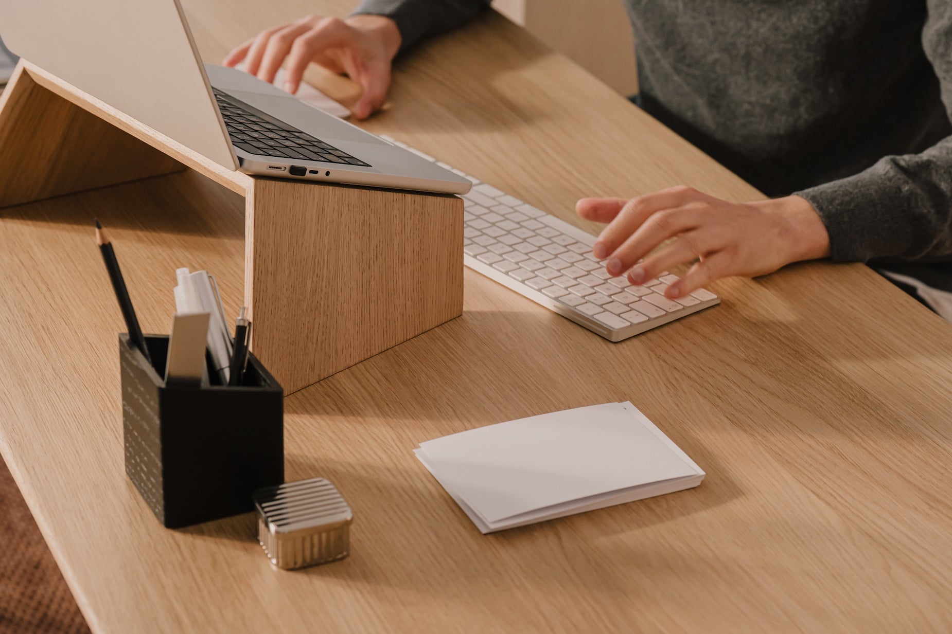 Person using a laptop and keyboard at a wooden desk with office supplies.  | light oak,