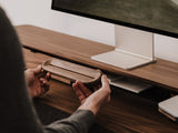 Person holding a wooden to-do desk stand in front of a computer monitor on a desk. | walnut