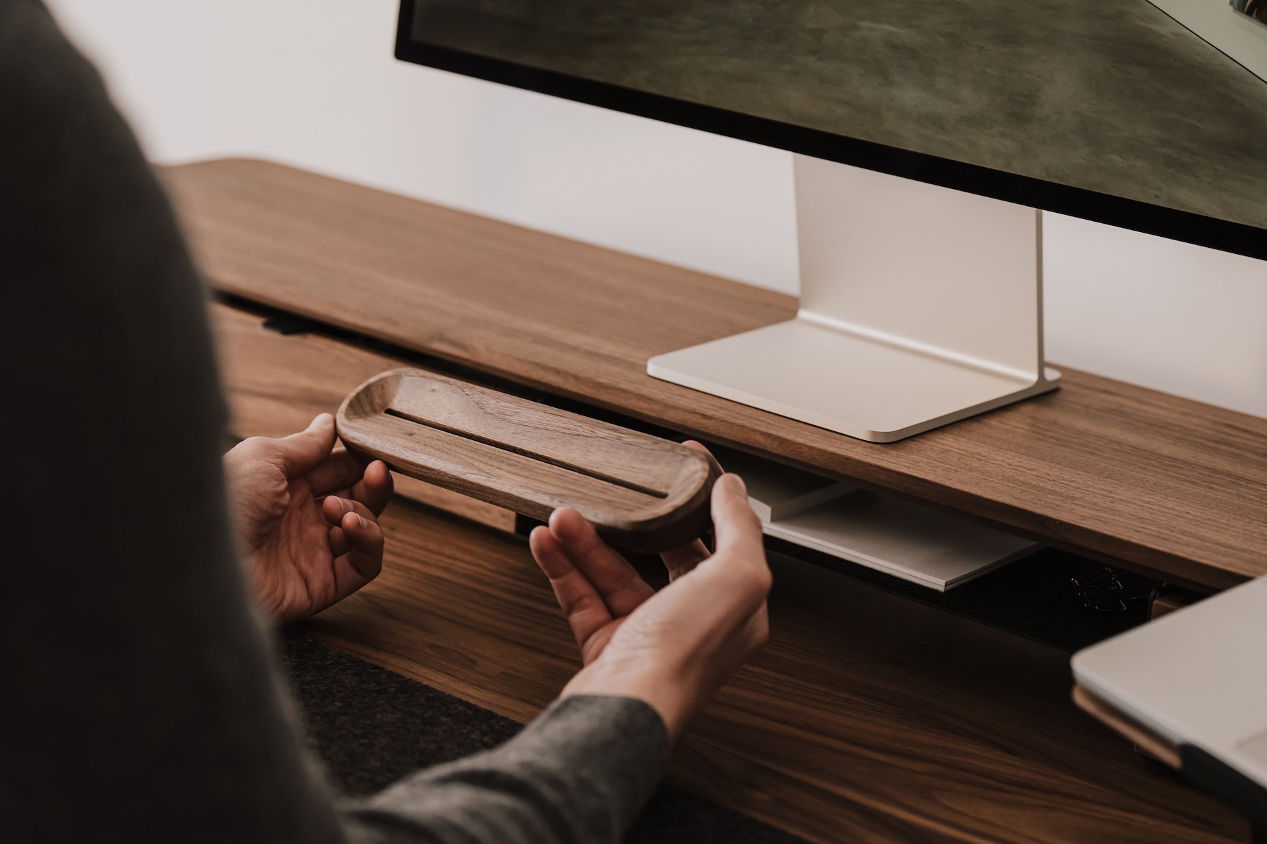 Person holding a wooden to-do desk stand in front of a computer monitor on a desk. | walnut