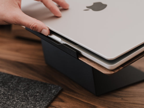 Person placing a laptop on a black stand with a wooden surface underneath Oakywood Laptop Riser | walnut,