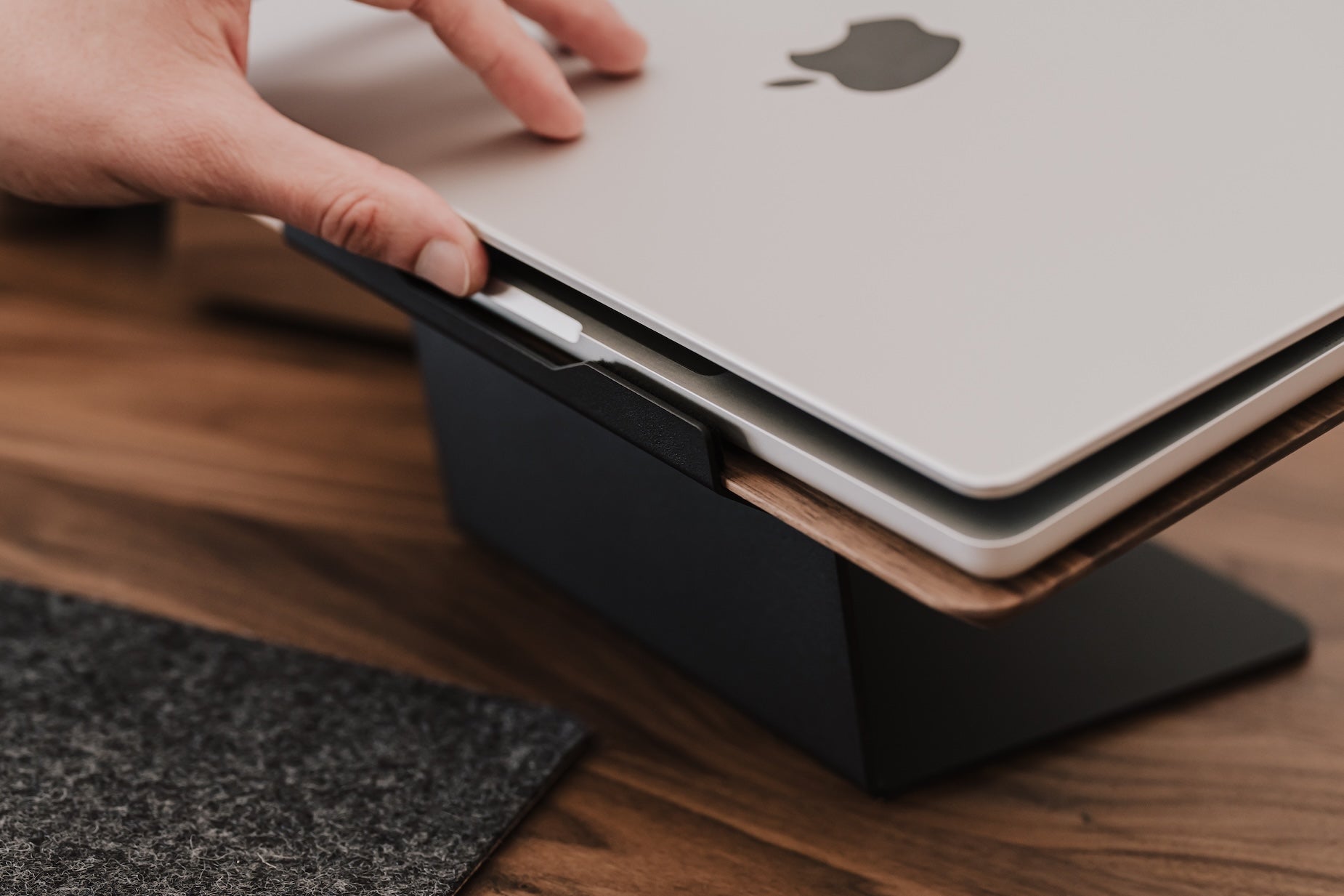 Person placing a laptop on a black stand with a wooden surface underneath Oakywood Laptop Riser | walnut,