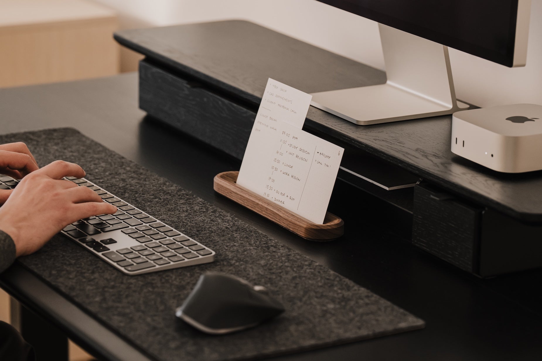 Person using a computer keyboard at a desk with a monitor and small stand holding a to-do list | walnut