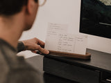 Person holding a to-do list made of paper on a desk next to a computer monitor | walnut