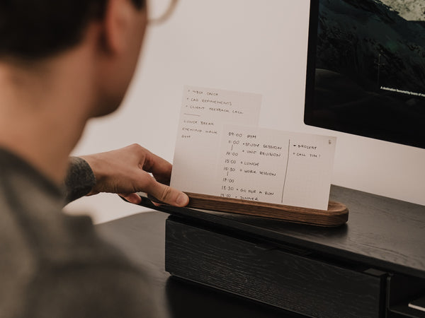 Person holding a to-do list made of paper on a desk next to a computer monitor | walnut