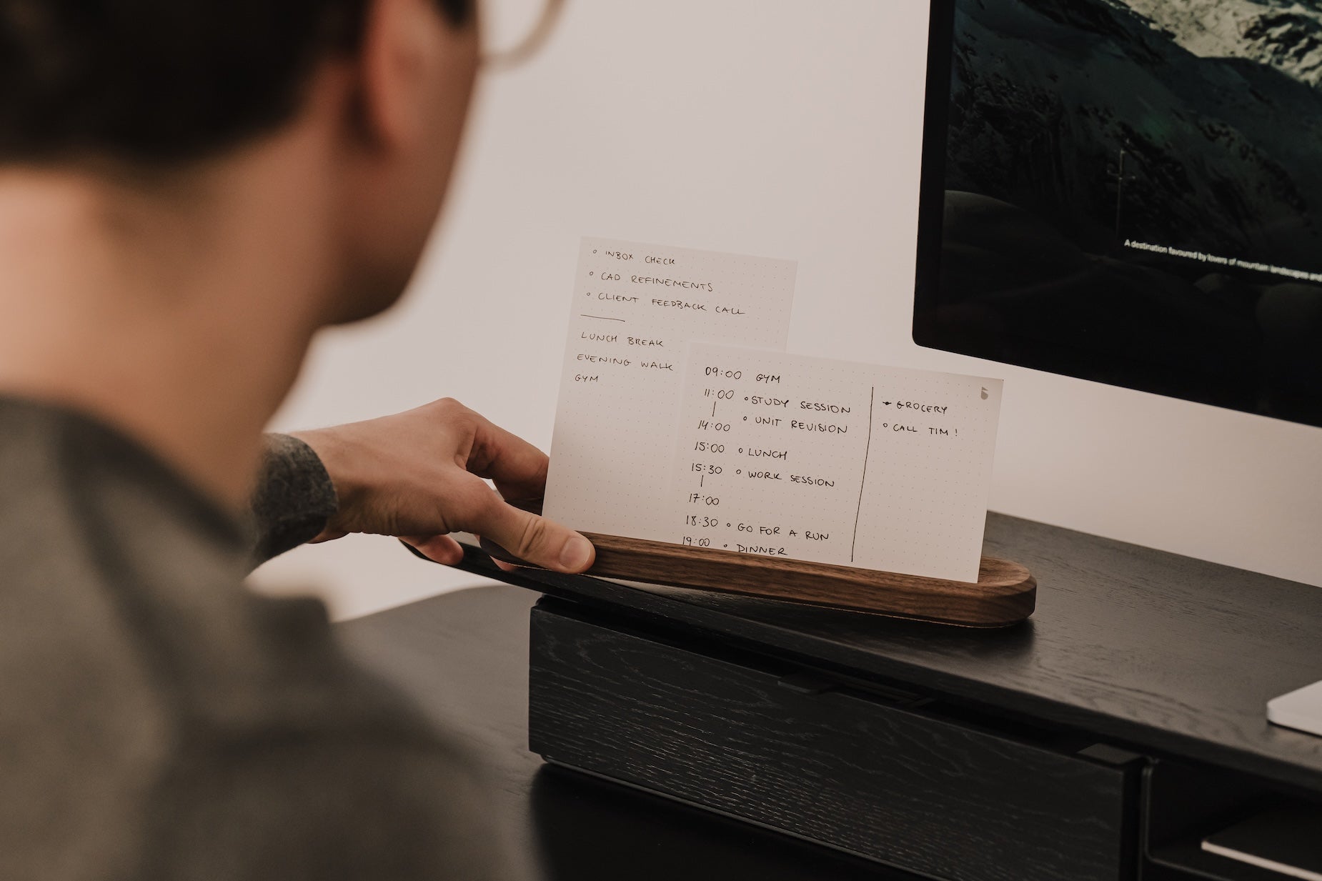 Person holding a to-do list made of paper on a desk next to a computer monitor | walnut