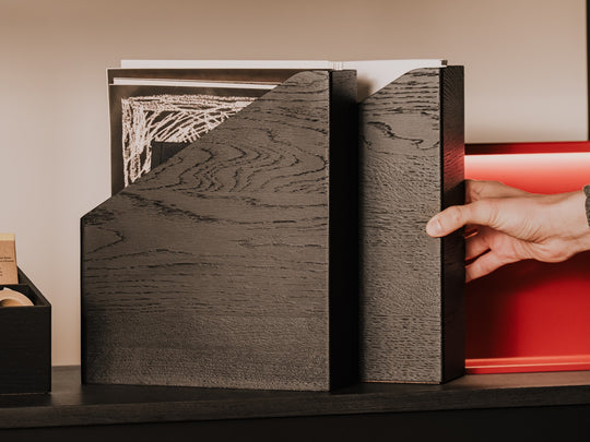 Hand reaching for a wooden documents holder, revealing a white object inside | black