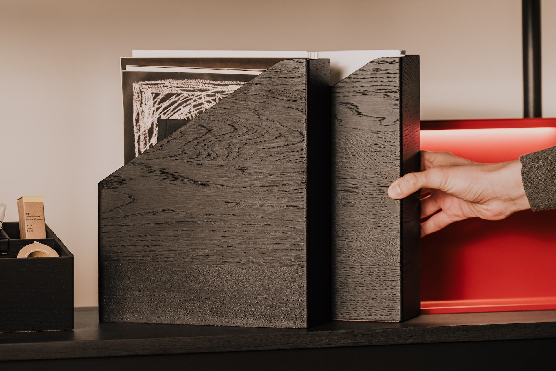 Hand reaching for a wooden documents holder, revealing a white object inside | black