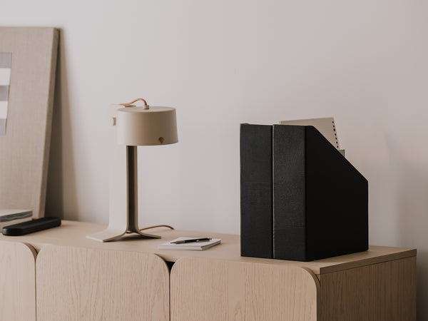 Modern office setup with a lamp, wooden magazine holder, and checkered poster on a wooden surface | black