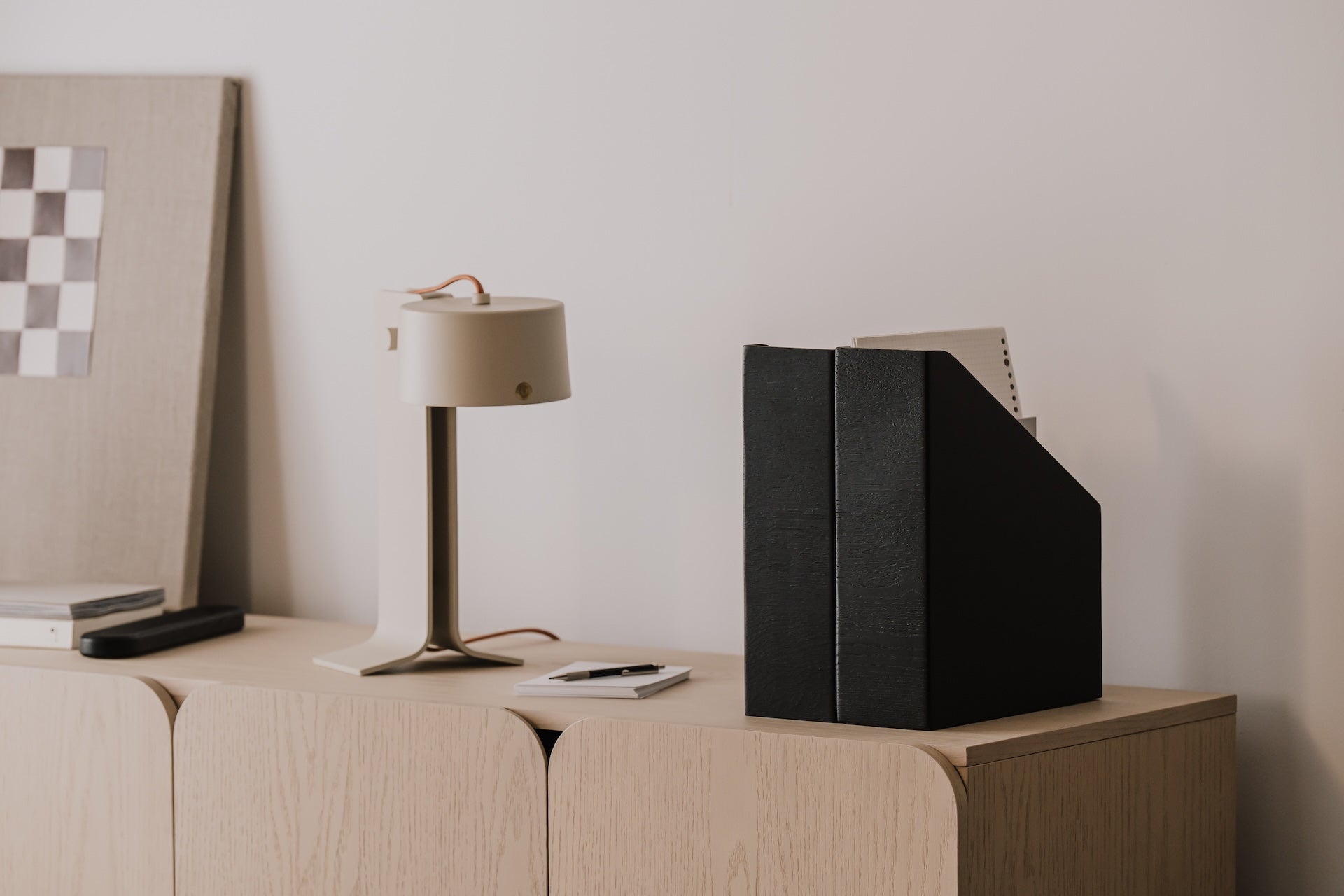 Modern office setup with a lamp, wooden magazine holder, and checkered poster on a wooden surface | black