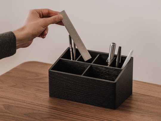 Person placing a card into a black desk organizer on a wooden surface | black