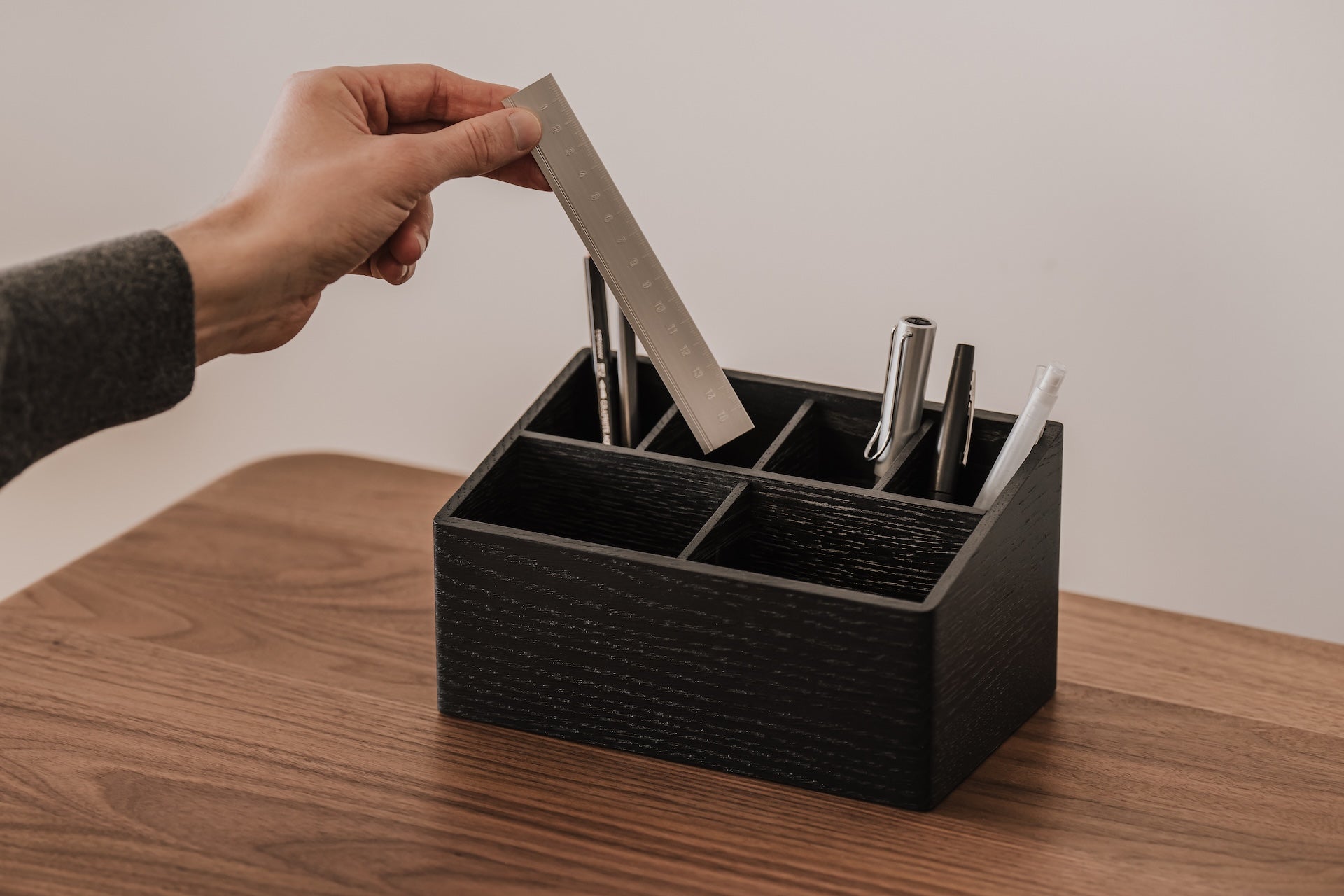 Person placing a card into a black desk organizer on a wooden surface | black