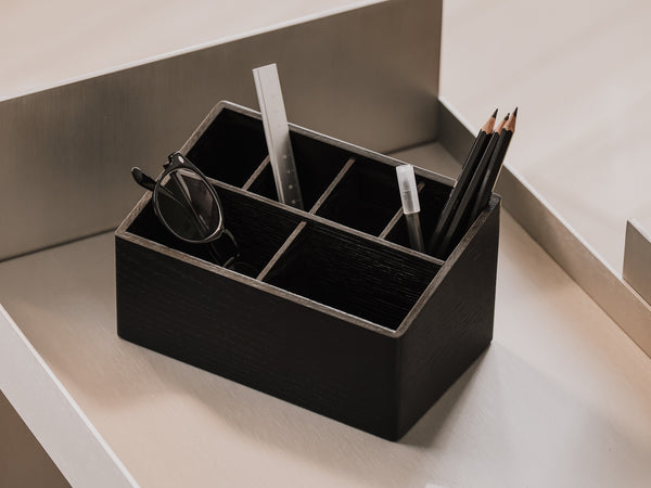 Black desk organizer with compartments organising glasses and pencils on a neutral stainless steel background | black