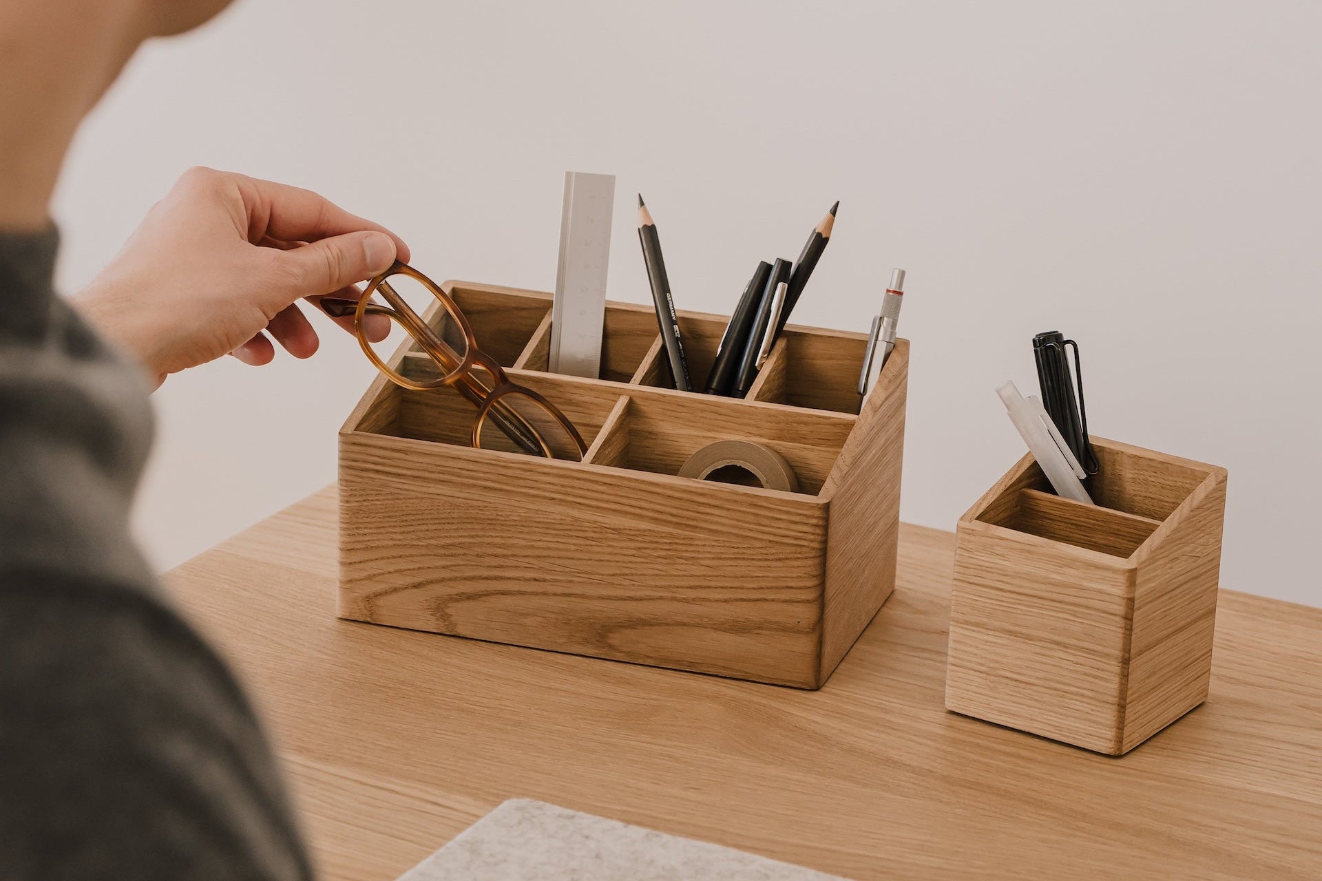 Person organizing stationery items in wooden desk organizers on a desk. | oak