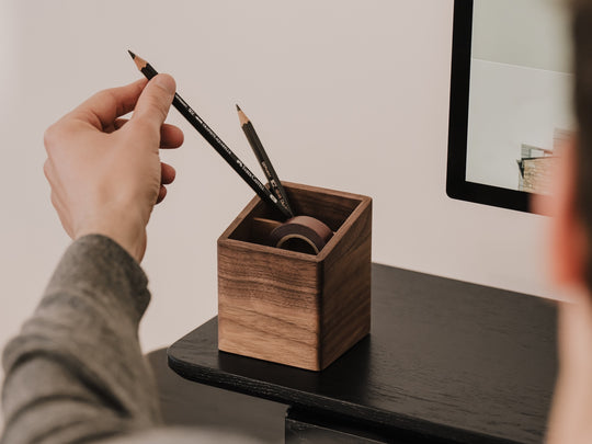 Person placing a pencil into a wooden pen holder on a desk. | walnut