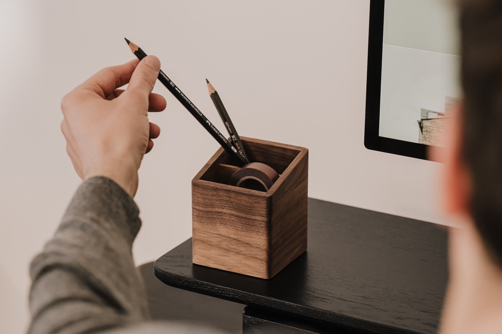 Person placing a pencil into a wooden pen holder on a desk. | walnut