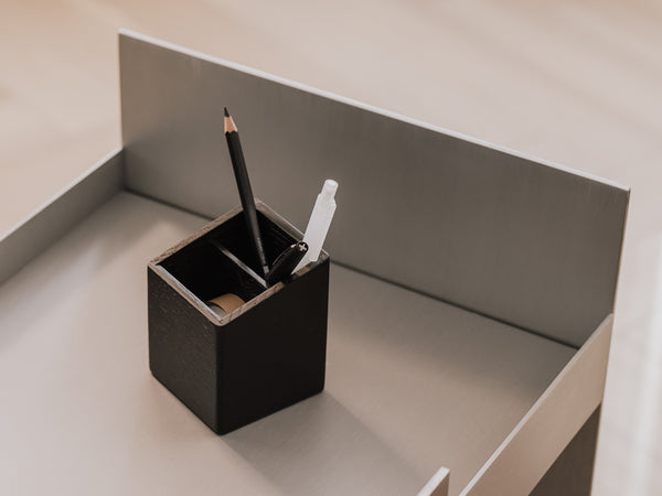 Black pen holder with a black pen and white eraser on a light gray surface | black