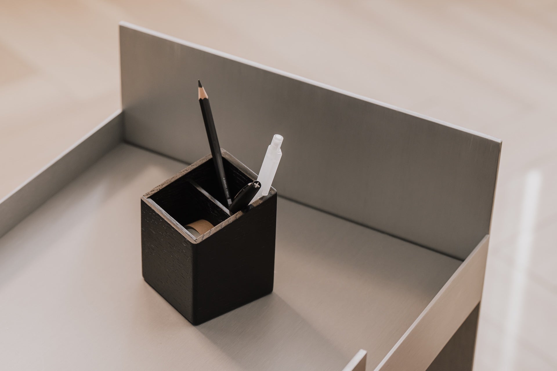 Black pen holder with a black pen and white eraser on a light gray surface | black