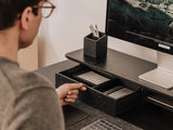 Person using a computer at a desk with a monitor, keyboard, and pen holder.   | black