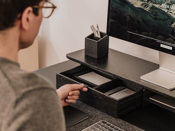Person using a computer at a desk with a monitor, keyboard, and pen holder.   | black