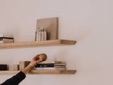 Person reaching for a wooden ball on a shelf against a plain wall | light oak