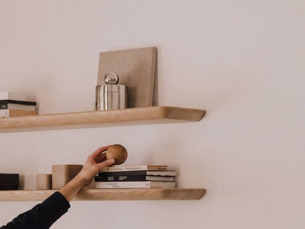 Person reaching for a wooden ball on a shelf against a plain wall | light oak